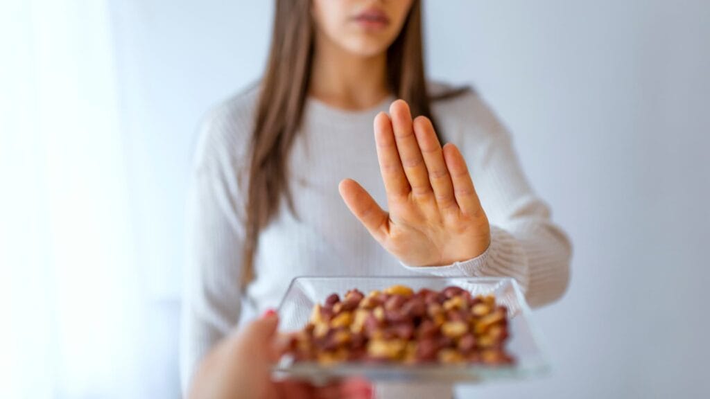 Image of a person being offered nuts and holding up a hand in response to say no thanks